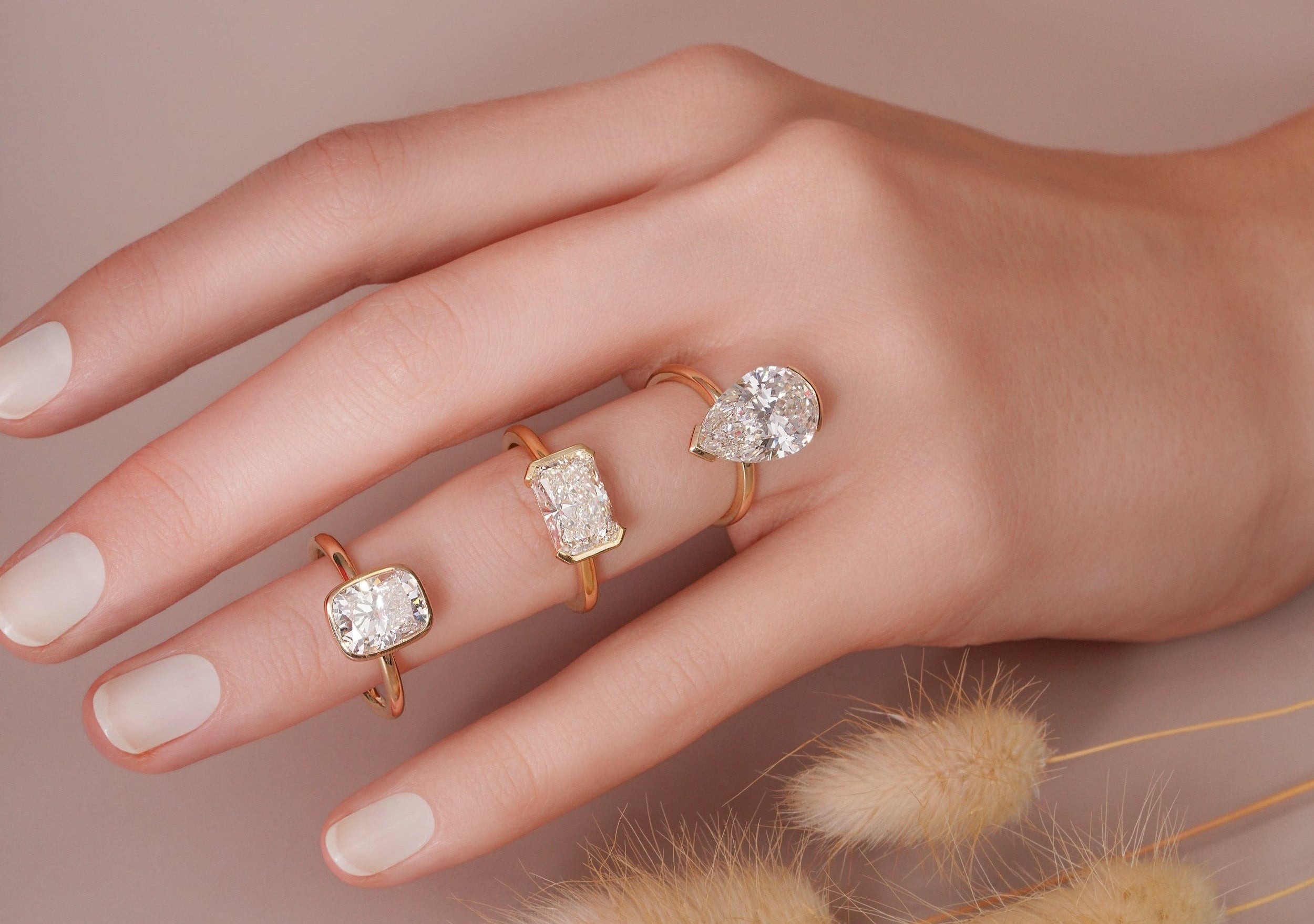 Hand wearing three gold rings with diamond accents on a neutral background